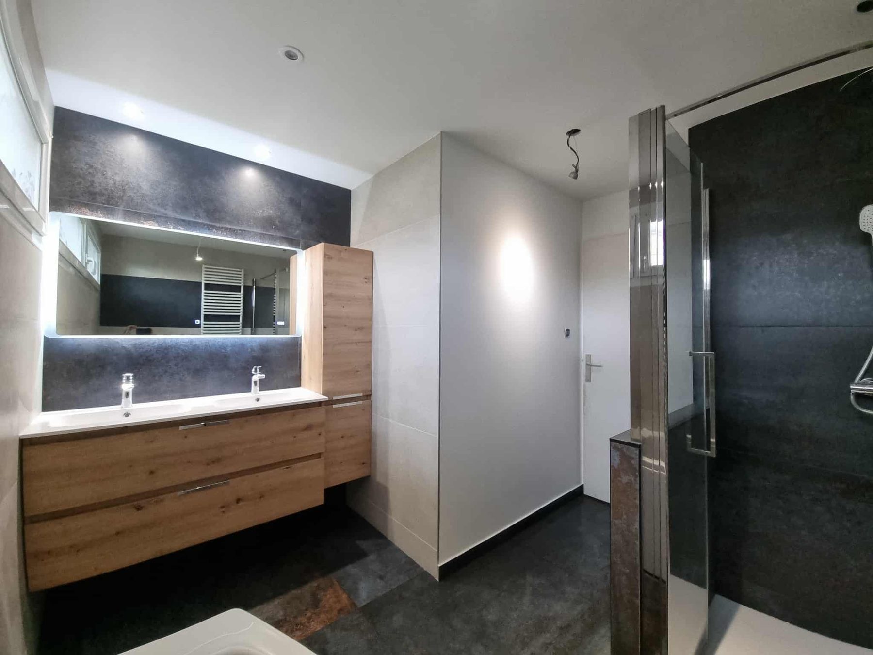 Double vasque en chêne devant un mur sombre, douche à l'italienne