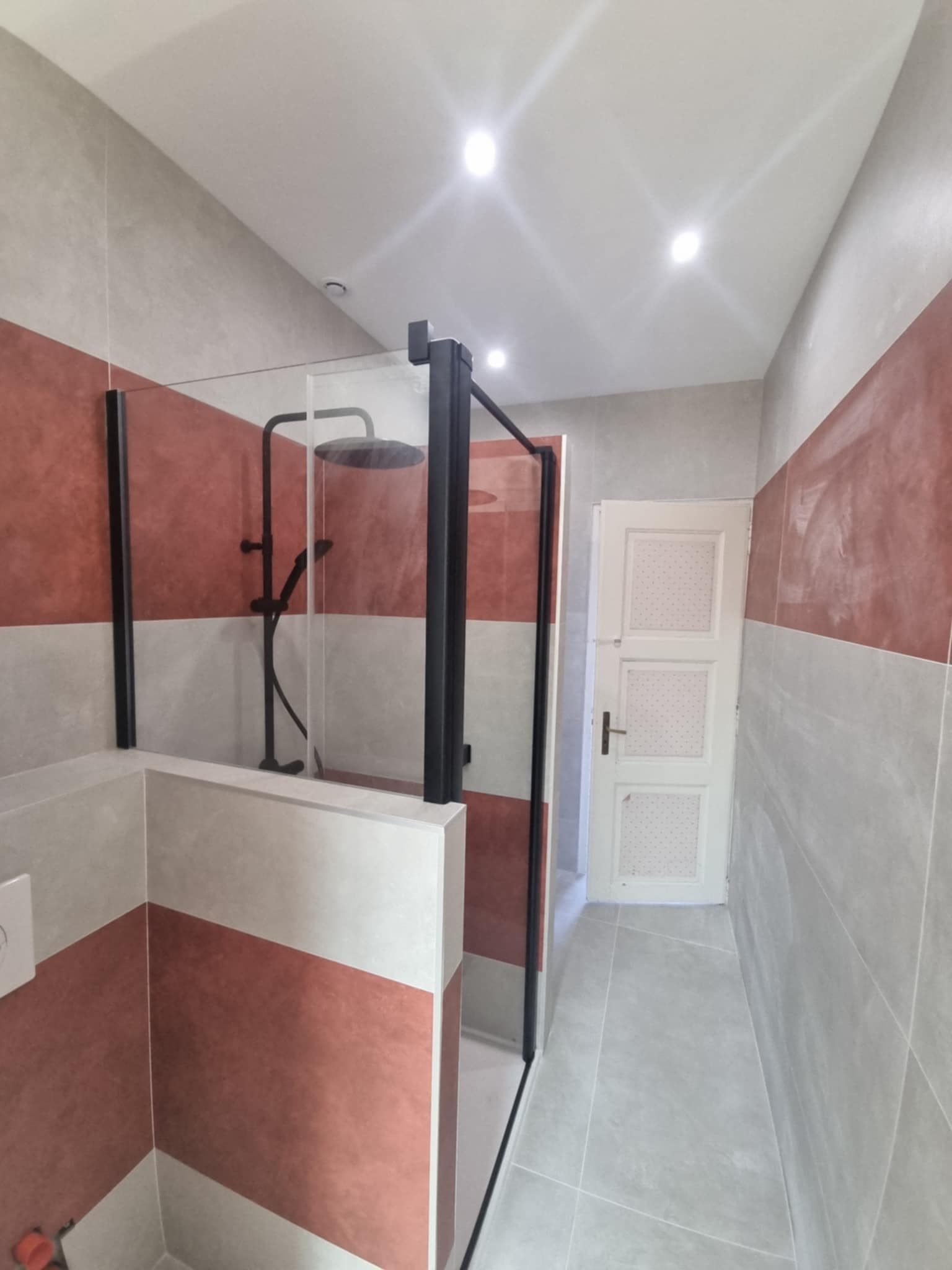 Douche à paroi noire et murs en bandes terre cuite