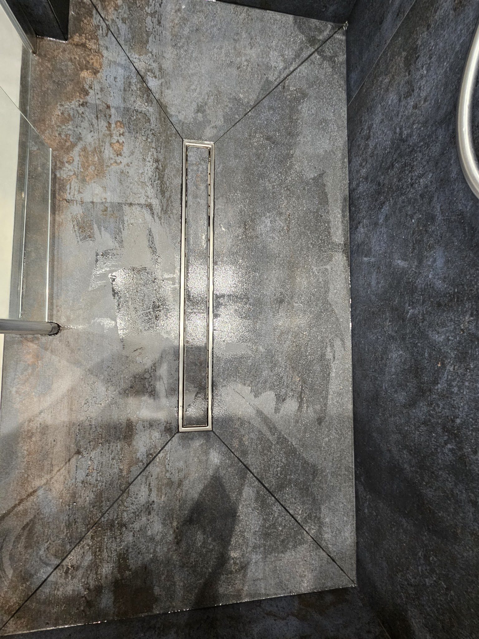 Sol de douche vu de dessus, carreaux coupés en quatre pans vers un caniveau inox